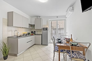 A modern kitchen with white cabinets, a built-in microwave, and a dining area with a wooden table and metal chairs. - Casa Vergolano (Arco)