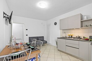 A modern kitchen with a dining area, white walls, and a grey sofa. - Casa Vergolano (Arco)