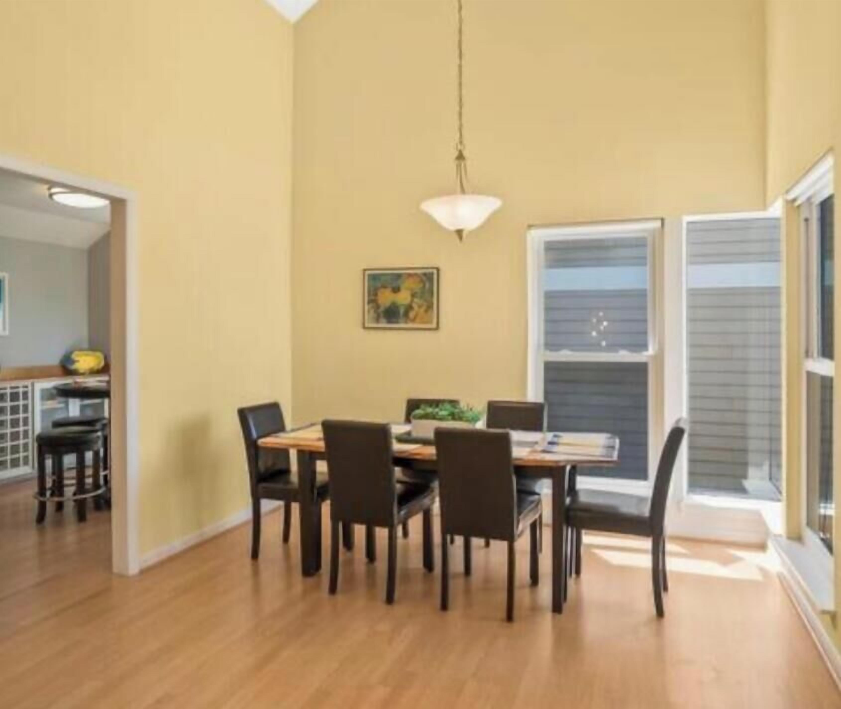 A dining area with a table and chairs, a hanging light fixture, and a painting on the wall.