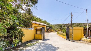 Uma entrada com portão fechado para uma propriedade, com muro amarelo, portão de metal e um caminho que leva a um edifício.