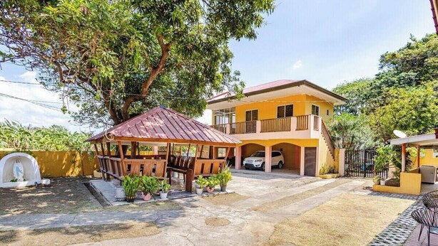 Uma casa de dois andares com uma varanda, uma área de estar coberta ao ar livre e um carro estacionado na entrada.
