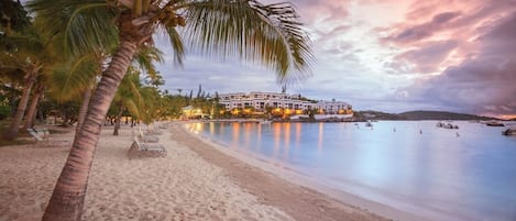 A beachfront hotel with a pool, palm trees, and a sunset view.