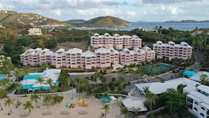 Ein Resort mit mehreren Gebäuden, einem Strandbereich mit Sonnenschirmen und Meerblick.