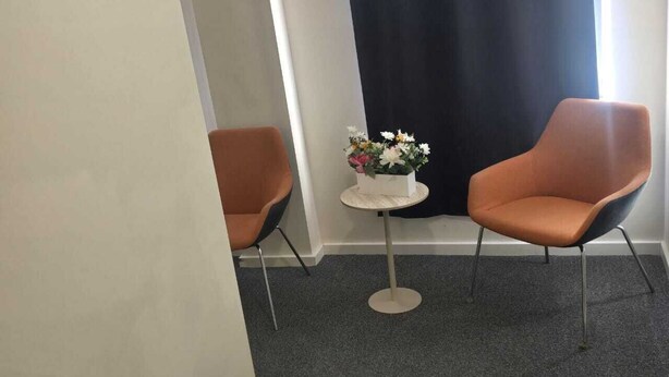 Una stanza con due poltrone arancioni, un tavolino rotondo con un bouquet di fiori e una tenda scura.