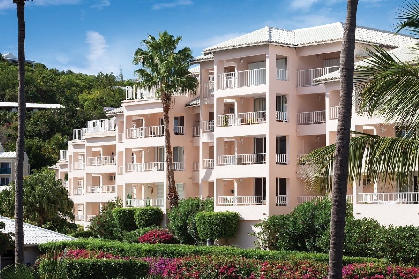 A multi-story hotel with balconies, surrounded by lush greenery and palm trees.