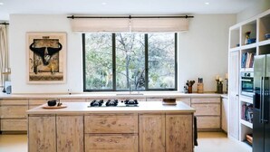 Une cuisine moderne dotée d’un grand îlot central, d’une fenêtre offrant une vue sur les arbres et d’une œuvre d’art accrochée au-dessus de l’îlot.