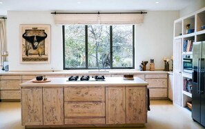 A modern kitchen with a large island, a window with a view of trees, and a mounted artwork above the island. - Arimuni House - Nature Retreat (Nairobi)