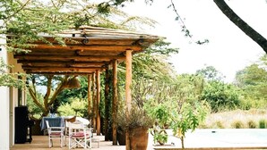 Une terrasse couverte, aménagée avec du mobilier d’extérieur, un piano et un grand bac à fleurs.