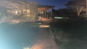 A nighttime view of a building with a covered patio, a pathway leading to the entrance, and a small pool.