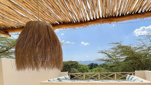A thatched roof structure, a cushioned seating area, and a view of greenery and mountains.
