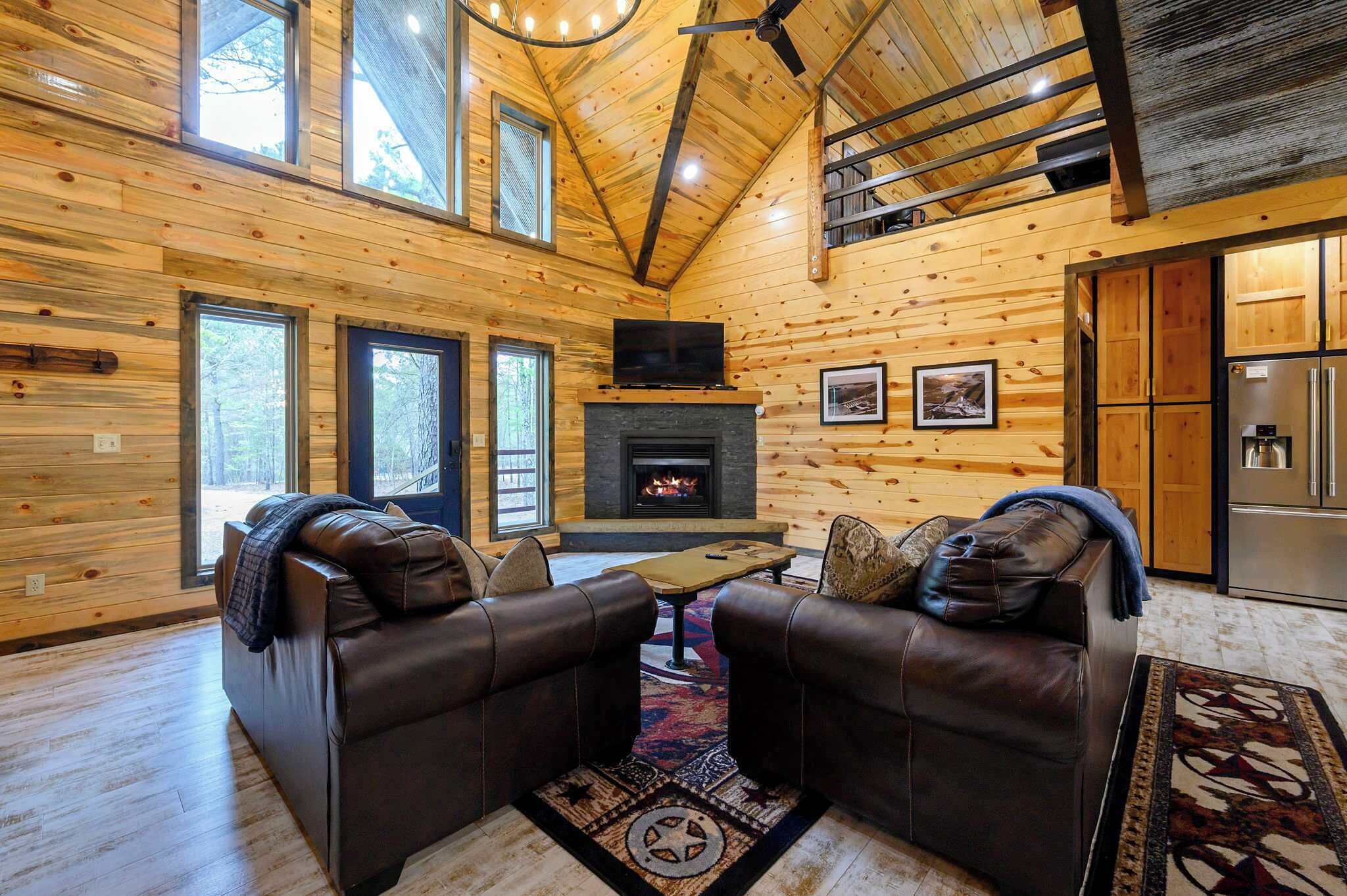 A log cabin interior with a fireplace, leather sofas, and a dining area.