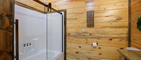 Une salle de bain aux murs lambrissés, dotée d’une douche en verre, de toilettes blanches et d’un meuble-lavabo en bois.