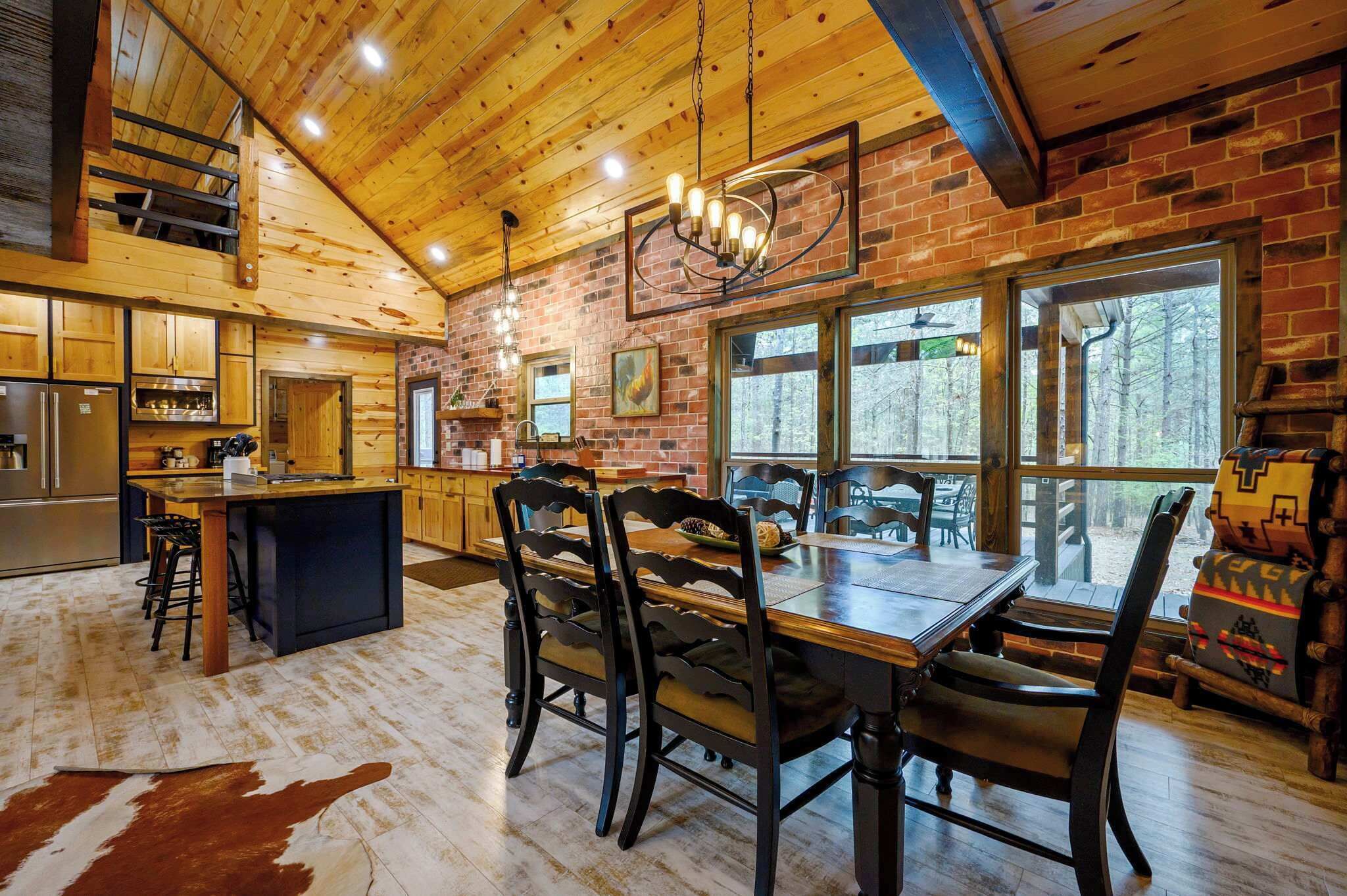 A rustic cabin interior with a kitchen, dining area, and large windows.