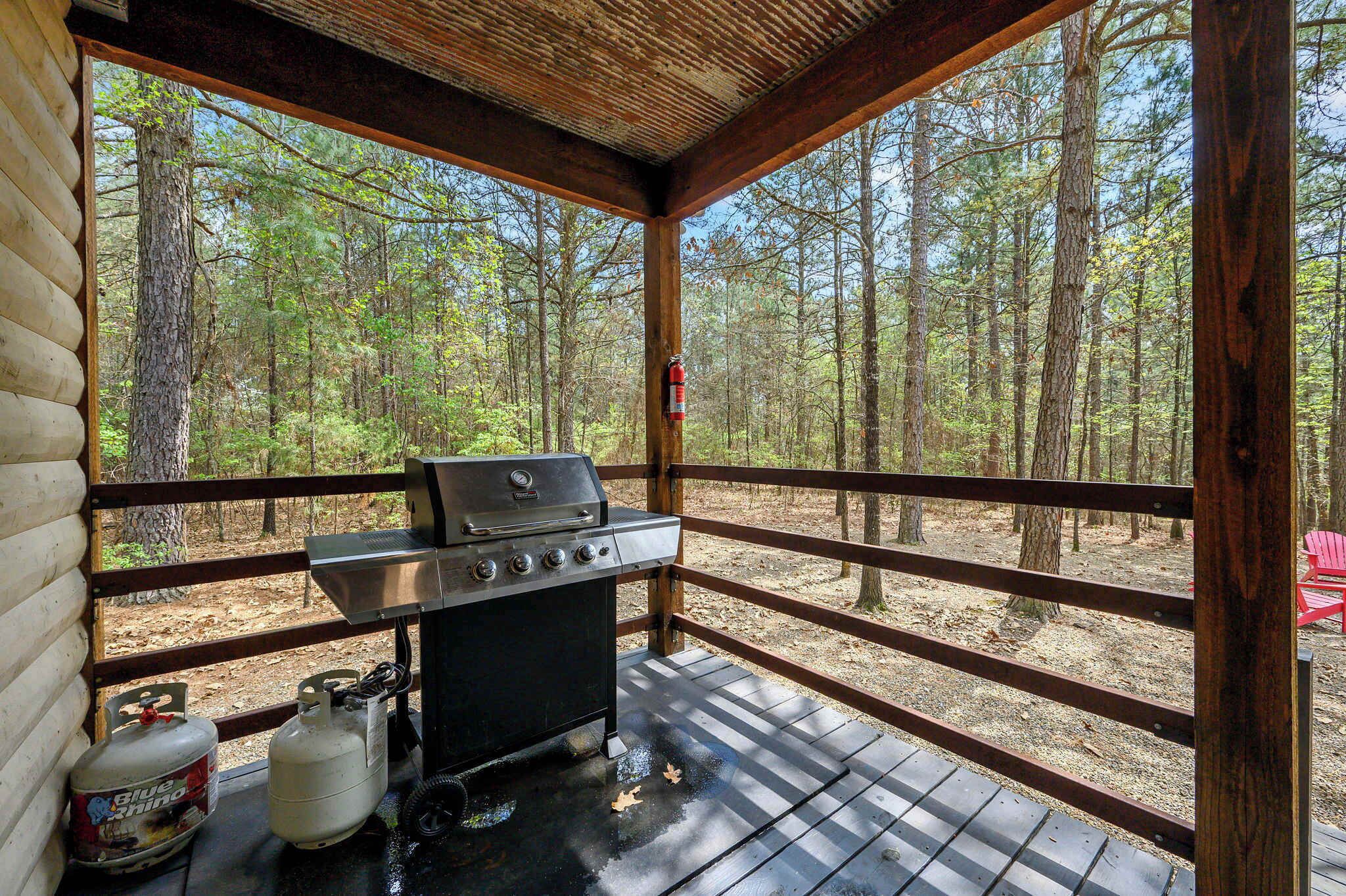 Un espace extérieur abrité, équipé d’un barbecue, d’une bouteille de propane et offrant une vue sur une forêt.