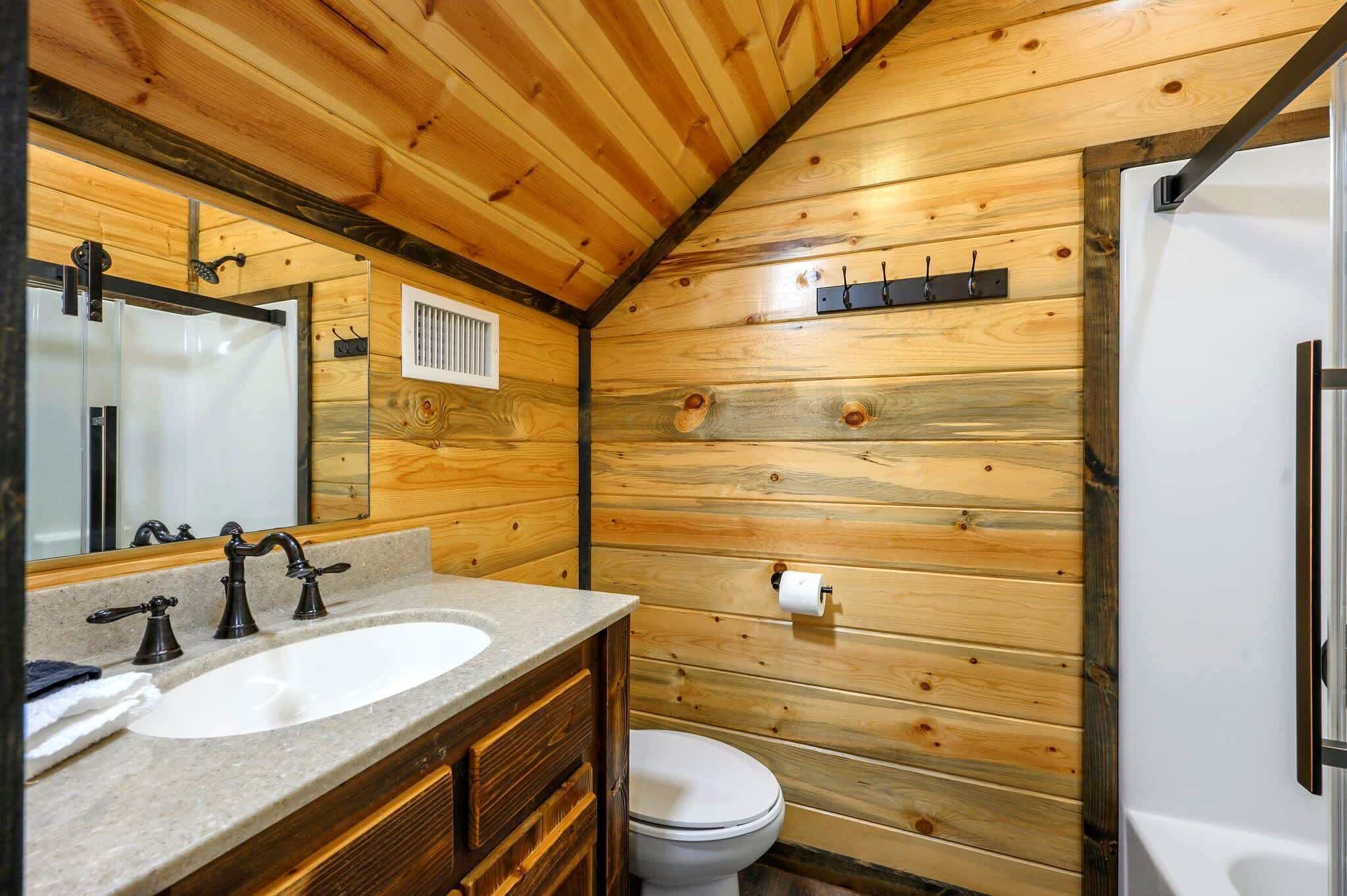 A wooden cabin bathroom with a sink, mirror, toilet, and shower.