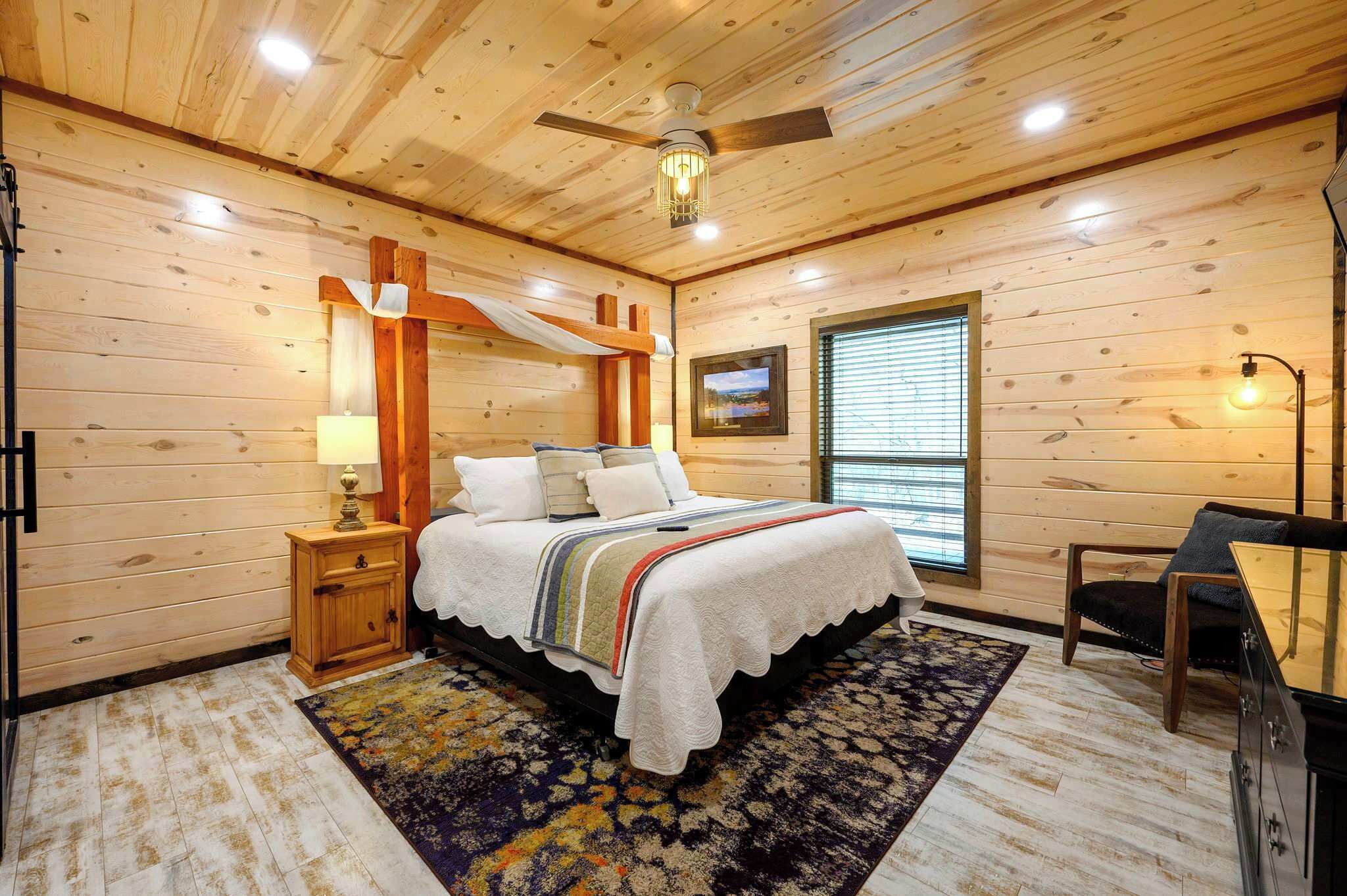 A wooden-paneled bedroom with a bed, bedside table, lamp, and a TV on the wall.