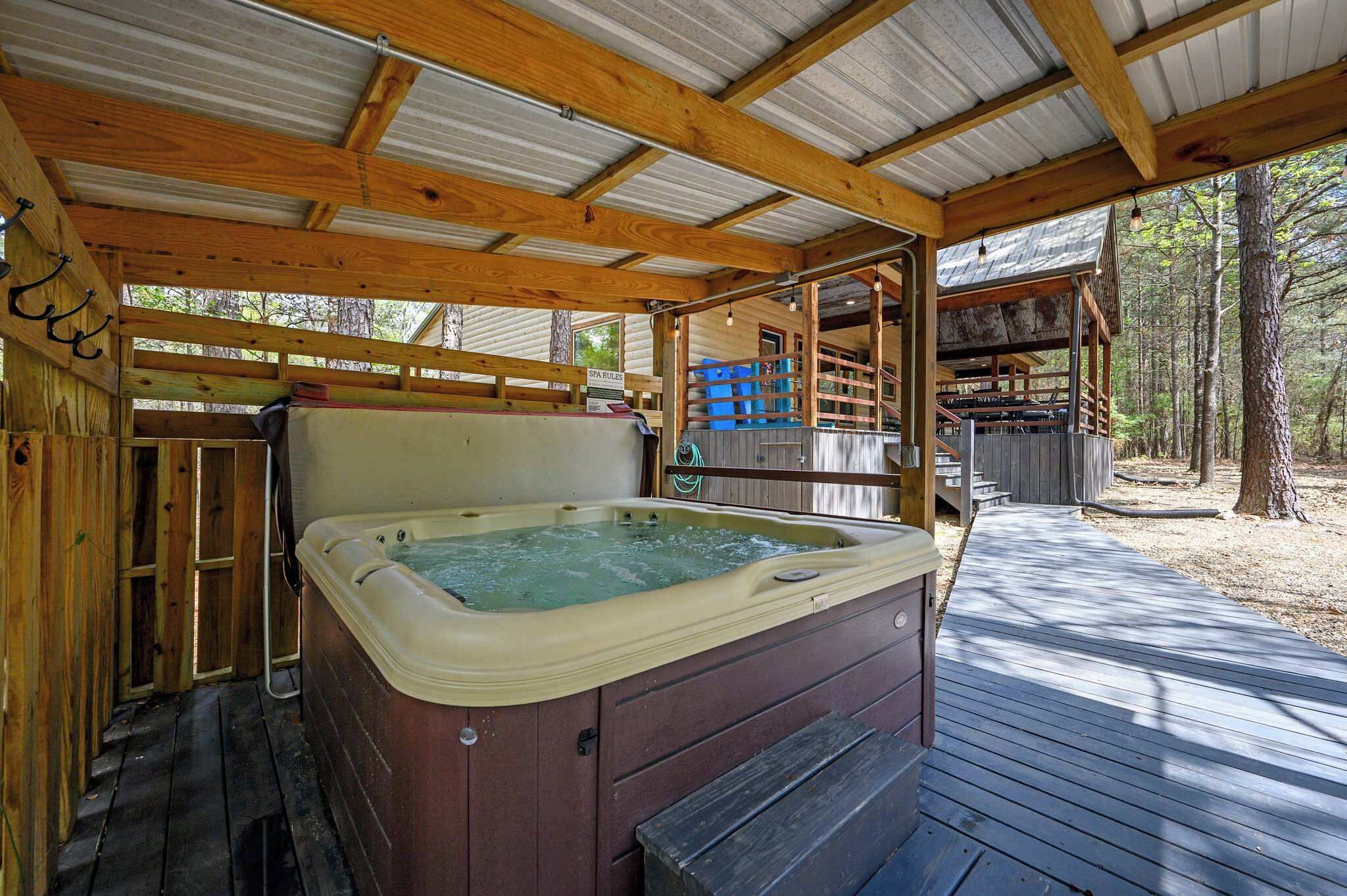 A hot tub under a wooden deck with a covered area, surrounded by trees.