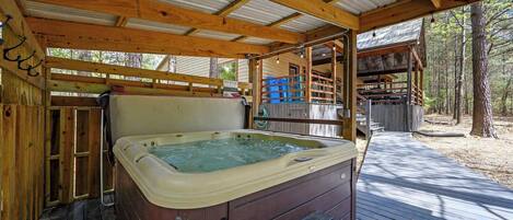 A hot tub under a wooden deck with a covered area, surrounded by trees.