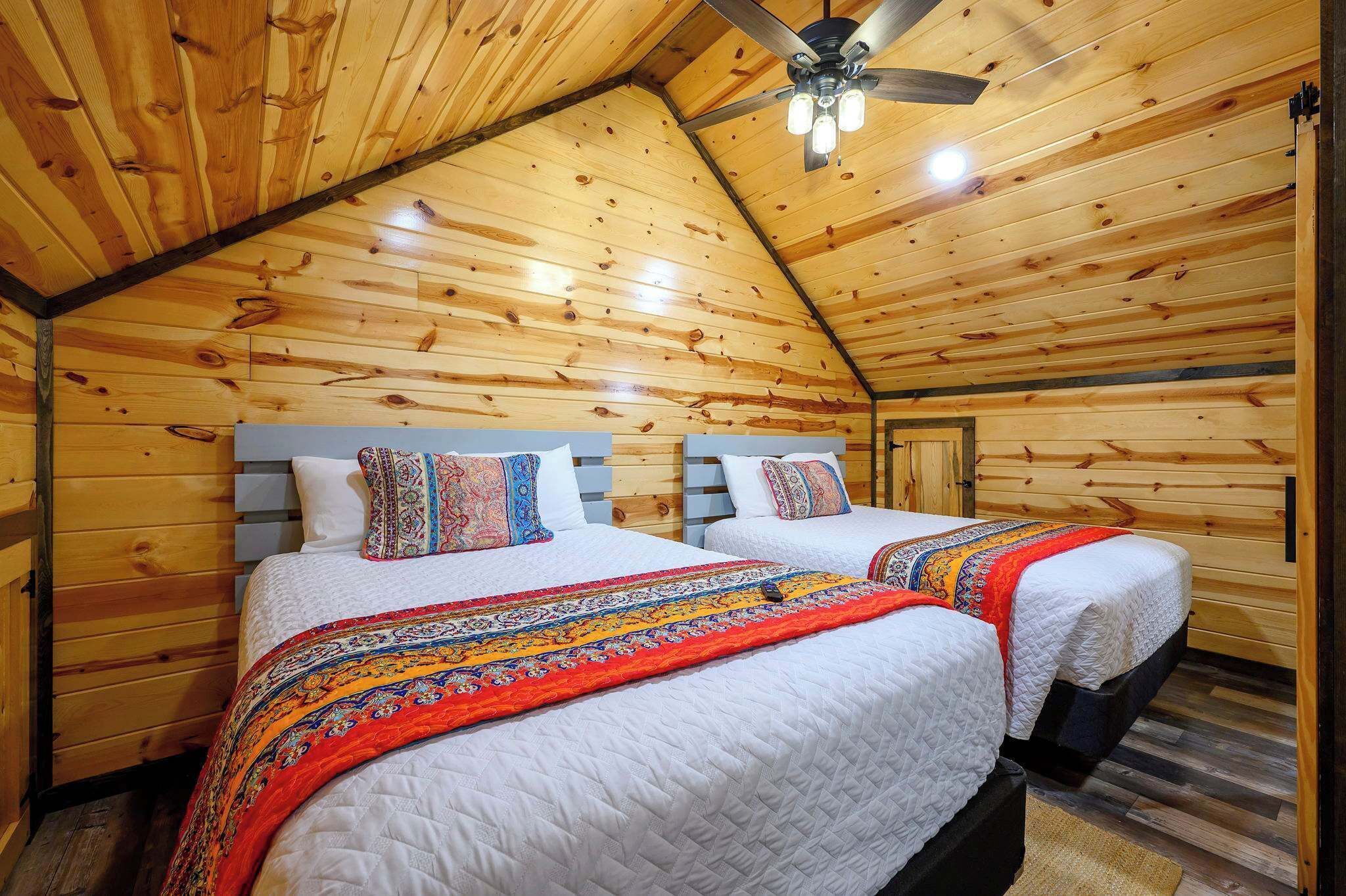 Una cabaña con dos camas, paredes de madera, techo inclinado y ventilador de techo.