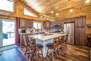 A spacious kitchen with wooden cabinets, a large island with bar stools, a stainless steel refrigerator, and a microwave. - Journey's End - 4BR Chalet • 7 Min to Attitash (Bartlett)