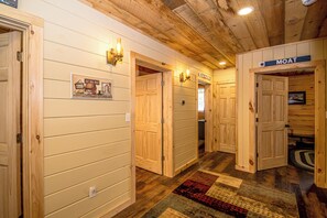 A wooden interior hallway with doors, a sign labeled 'MOAT,' and a patterned rug on the floor. - Journey's End - 4BR Chalet • 7 Min to Attitash (Bartlett)