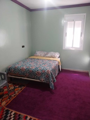 A bedroom with a bed, a window, and a carpeted floor. - Berber Family (Tilmi)