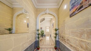 A corridor with stone walls, tiled flooring, and potted plants.