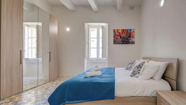 A bedroom with a bed, a nightstand, a wardrobe, and a door leading to another room.