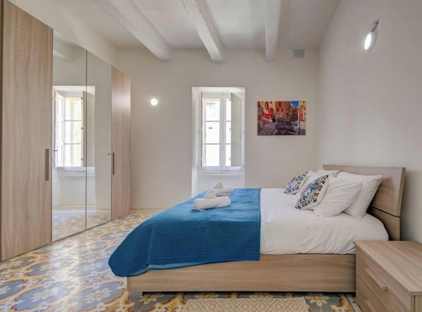 A bedroom with a bed, a nightstand, a wardrobe, and a door leading to another room.