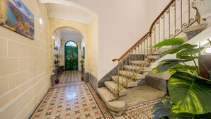 A hallway with a tiled floor, a staircase with a metal railing, and a green door at the end.