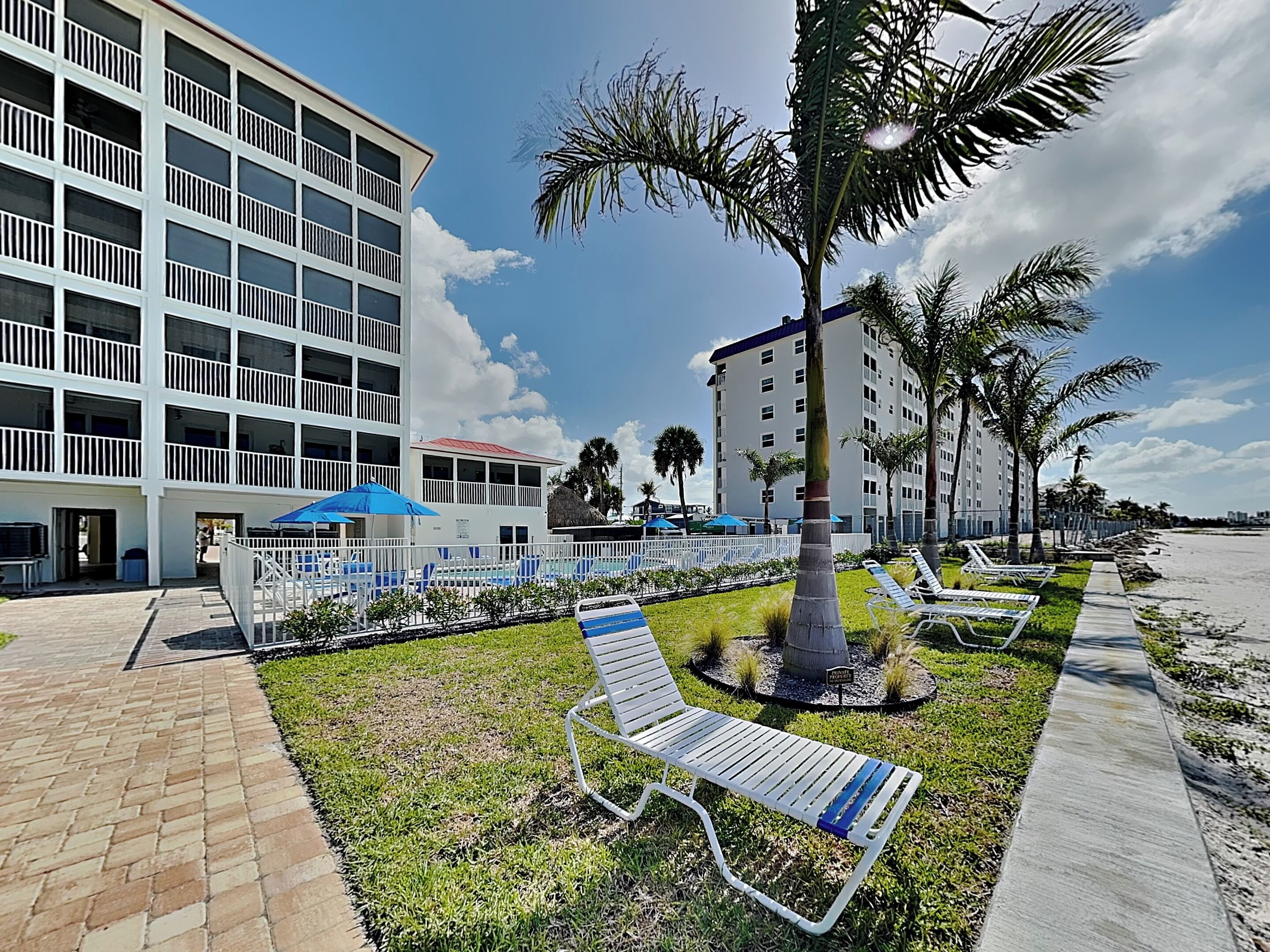 A hotel with a pool area, palm trees, and a brick pathway.