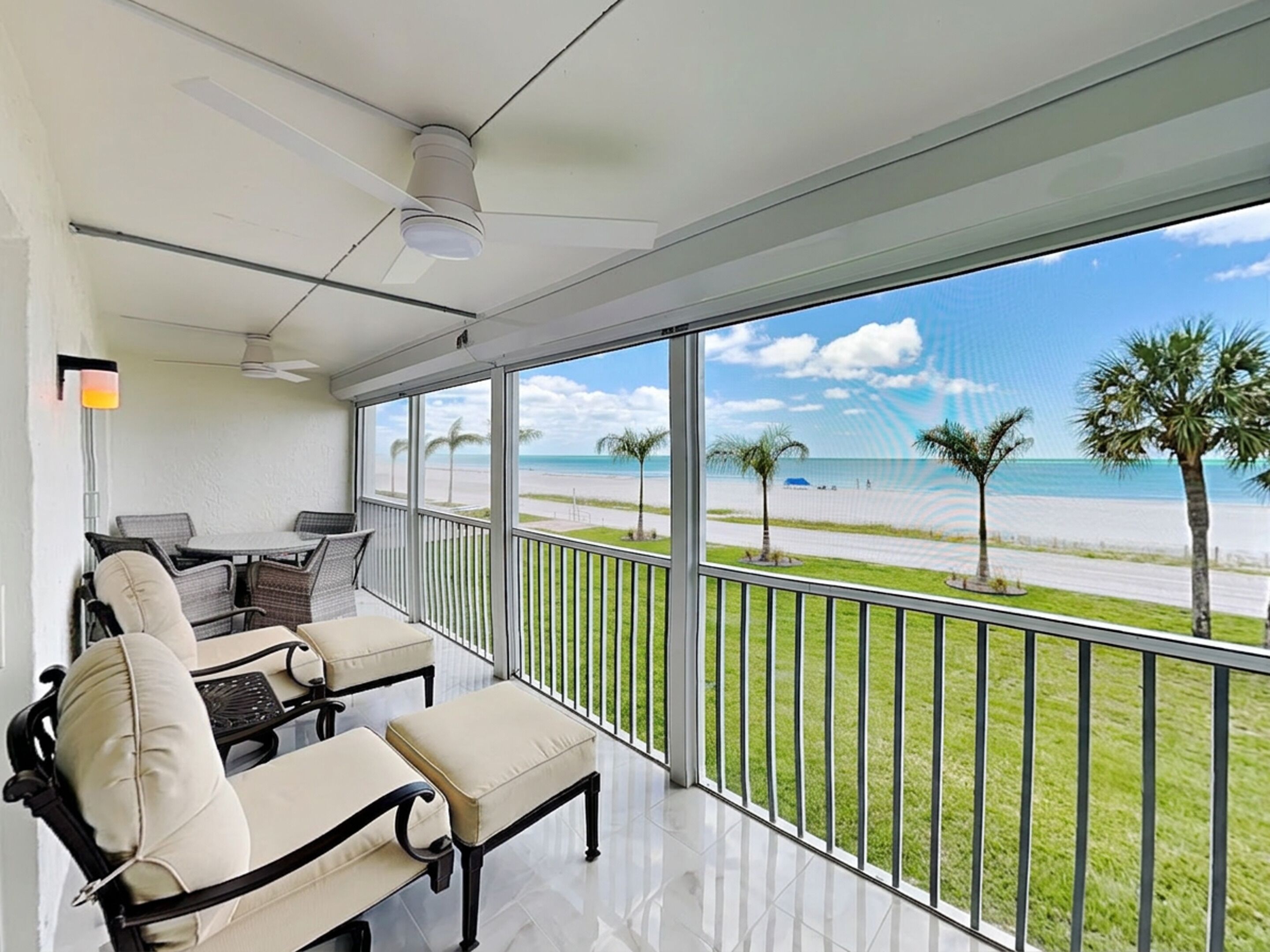 A balcony with a view of the beach, a table with chairs, and a ceiling fan.