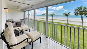 A balcony with a view of the beach, a table with chairs, and a ceiling fan. - Pointe South 105 | Gulf-Front + Newly Updated (Fort Myers Beach)
