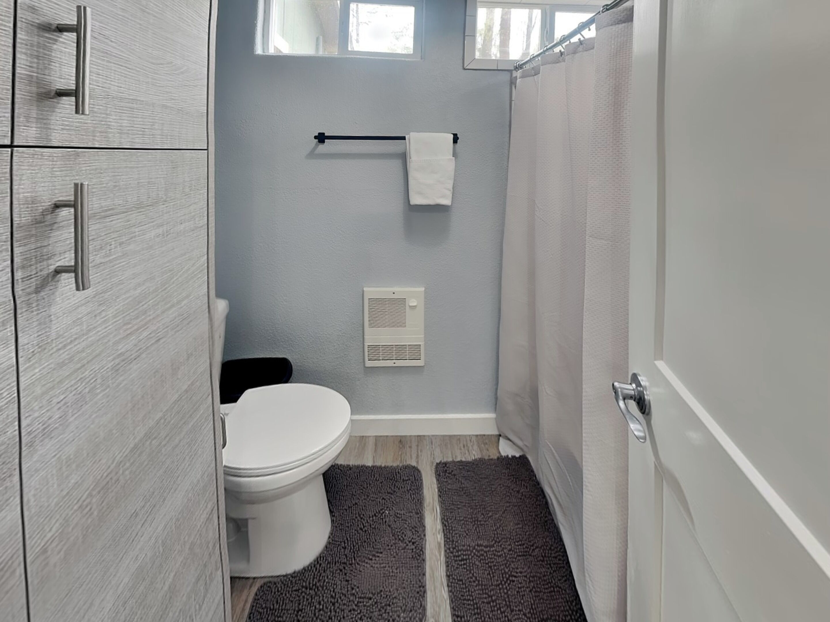 Un baño con inodoro, toallero, cortina de ducha y un respiradero en la pared.