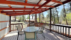 Une terrasse en bois avec une table et des chaises en verre, entourée d’une rambarde en métal.