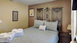 Un lit bien fait, recouvert d’une couvre-lit à motifs, avec une tête de lit ornée de motifs métalliques et une table de chevet surmontée d’une lampe.