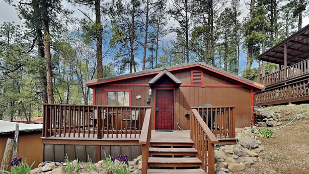 Une cabane avec une porte rouge, une terrasse en bois et un escalier menant à l’entrée.