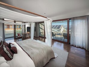 Een slaapkamer met een groot bed, een balkon met een tafel en stoelen, en uitzicht op gebouwen.