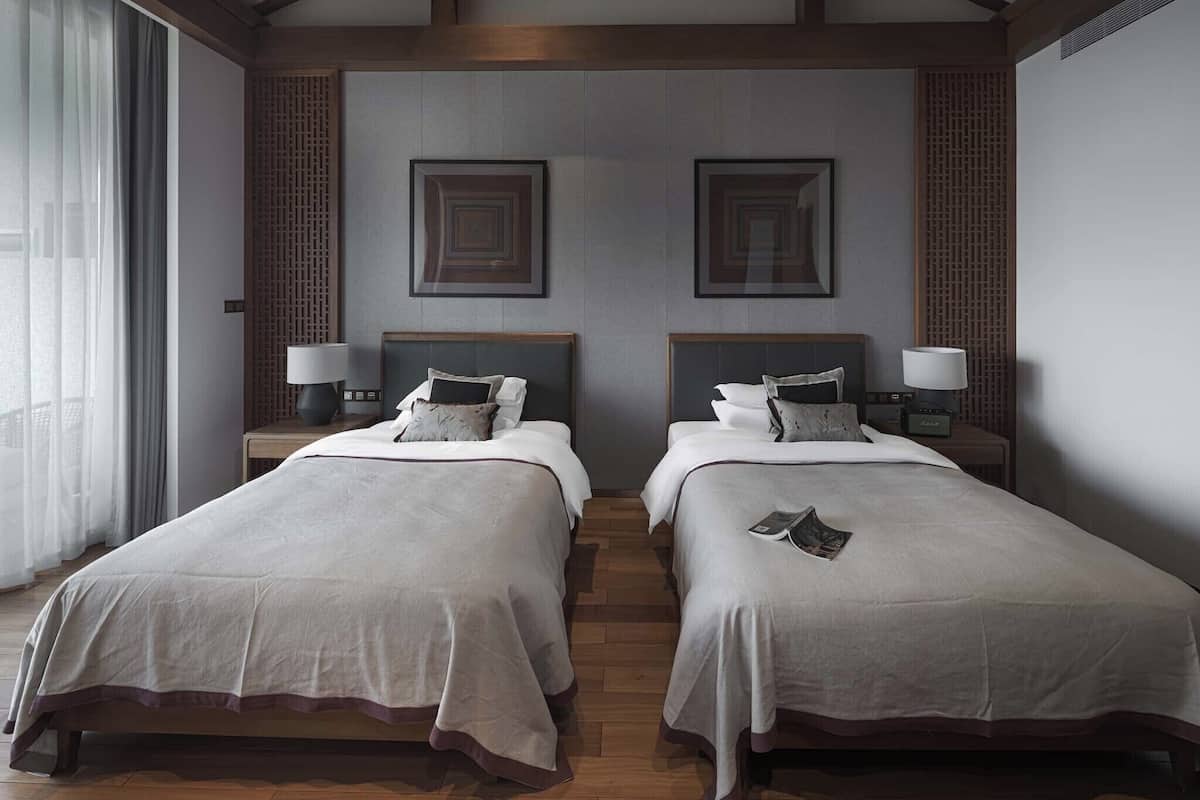 A hotel room with two beds, wooden beams on the ceiling, and a large window with curtains.