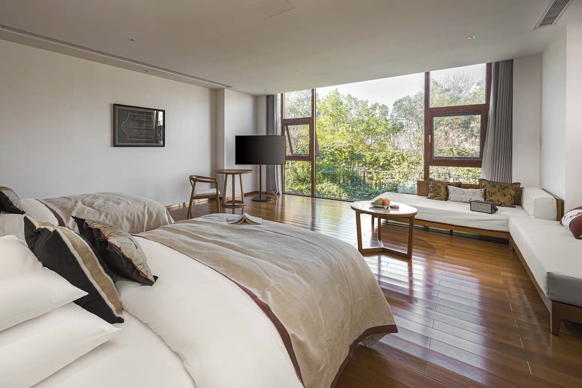 A spacious bedroom with a large bed, a sofa, a TV, and a view of the outdoors.