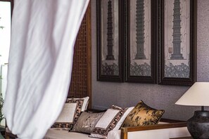 Een slaapkamer met een bed, nachtkastje, lamp en lijstjes met kunstwerken aan de muur.