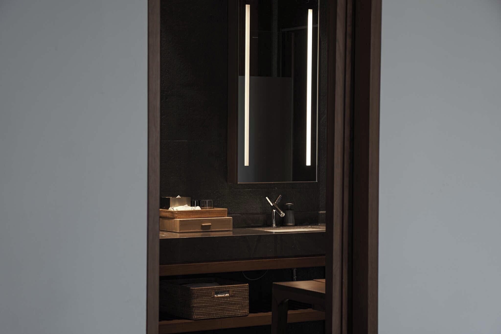 A modern bathroom with a dark wall, a mirror, a sink, and a shelf with a basket and a box.