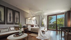 A bedroom with a four-poster bed, a sitting area with a sofa, a round coffee table, and a view through a large sliding glass door. - Arcadia Yunjinyue Hotel (Dali)