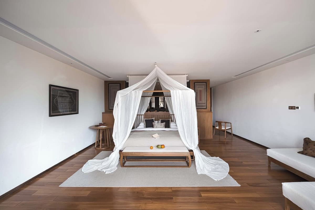 A bedroom with a canopy bed, wooden flooring, a small round table, and a sofa.