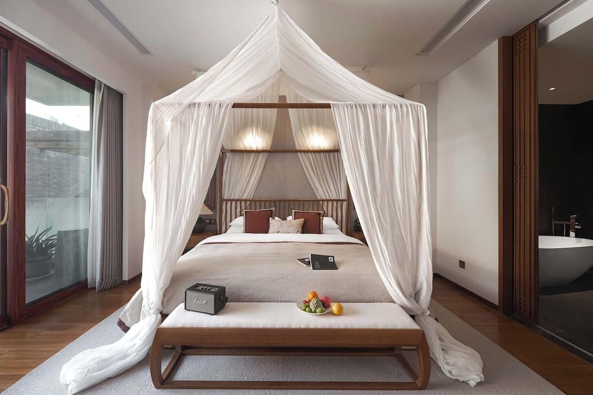 A four-poster canopy bed with a bedside table, a fruit bowl, and a radio.