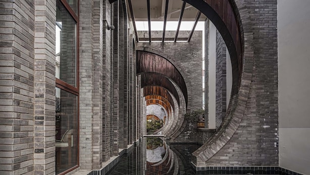 A corridor with brick walls, a reflective floor, and a wooden archway. - Arcadia Yunjinyue Hotel (Dali)