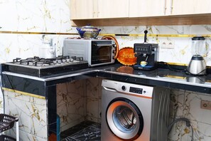 Een kleine keuken met een gasfornuis, magnetron, koffiezetapparaat en wasmachine.
