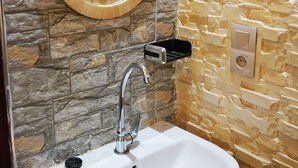 Ein Badezimmer mit Steinwand, Waschbecken in Weiß und einem Spiegel mit Holzrahmen.