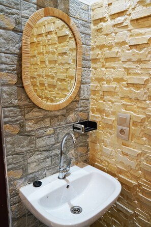 Un baño con pared de piedra, un lavabo blanco y un espejo con marco de madera.