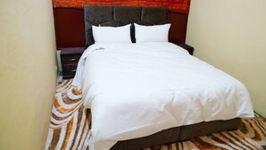Ein Bett mit weißer Bettwäsche, einem dunklen Kopfteil und einem gemusterten Teppich.